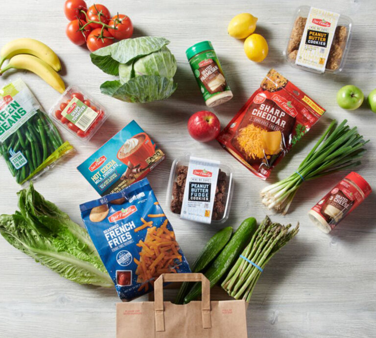 A table filled with groceries from Our Family including fruits, vegetables, cookies, cheese, hot cocoa mix, beans, and french fries.