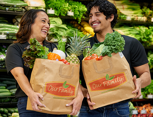 Two individuals with bags of fruits and vegetables in a grocery store.